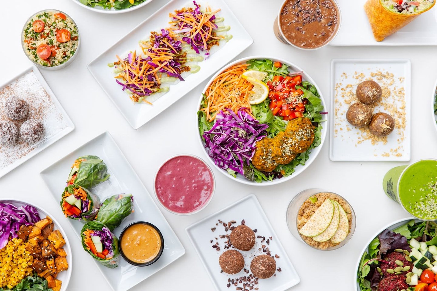 A spread of E+ROSE dishes — bowls, salads, spring rolls, booster bites, and smoothies